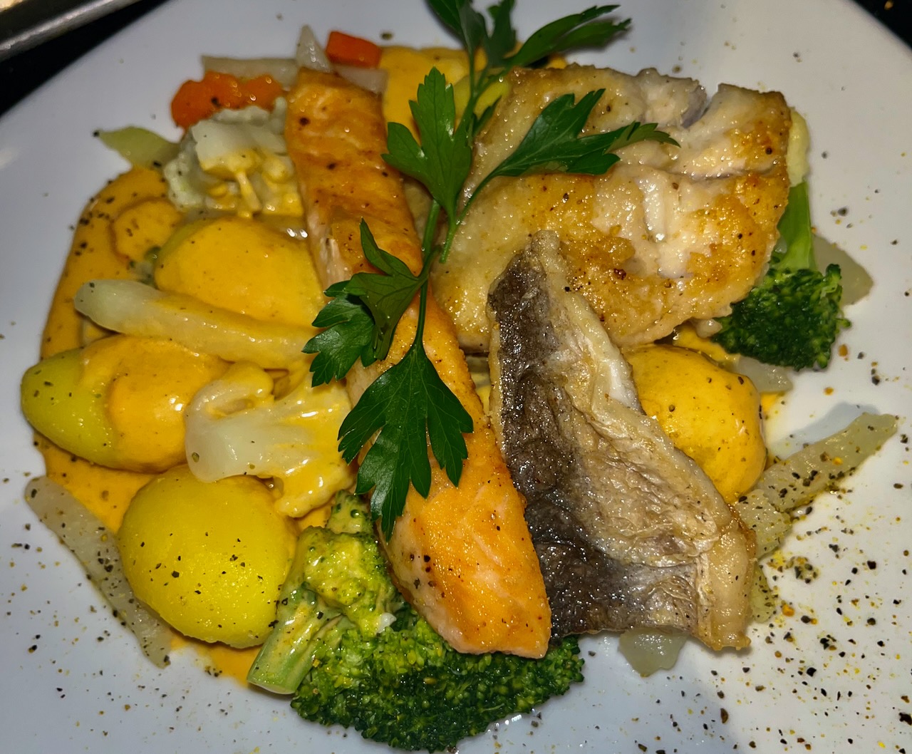 Ein Stück Lachs angerichtet auf Gemüsenudeln mit einm Limonenspalt und etwas frischem Blattspinat